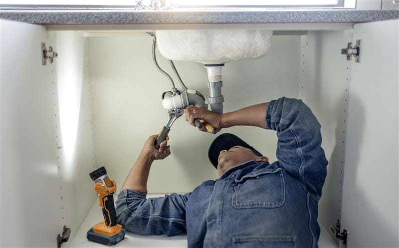 Plumber repairing pipes beneath a bathroom sink in Melbourne