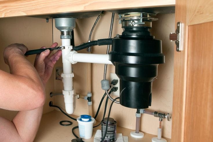 Plumber installing a garbage disposal beneath a kitchen sink in Melbourne
