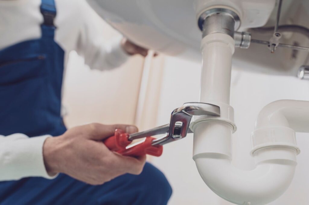 Plumber repairing a white drain pipe beneath a sink in Melbourne