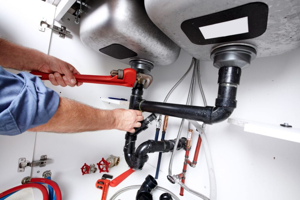 Plumber repairing drain pipes beneath a kitchen sink in Melbourne